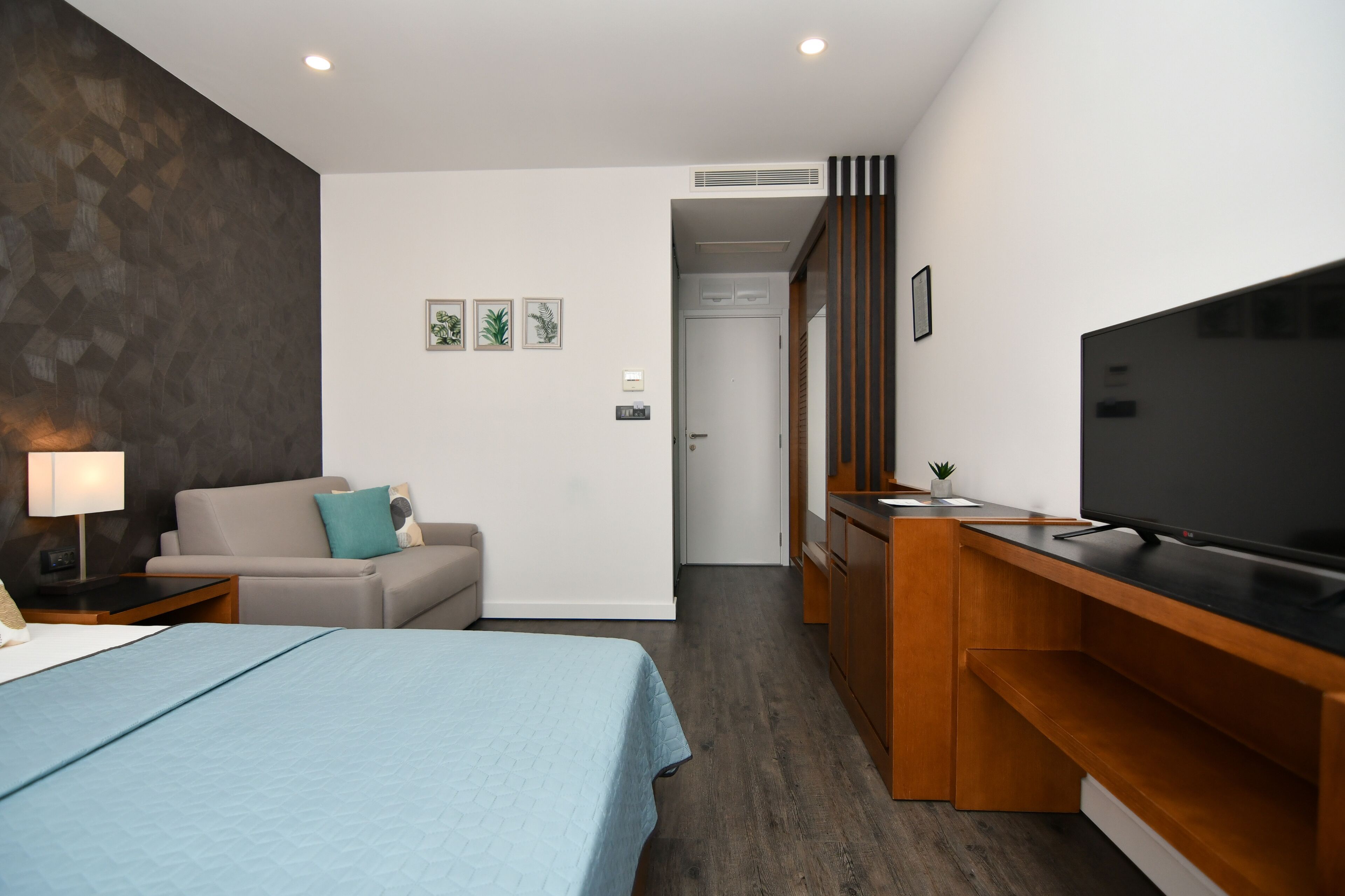 Una camera d'albergo con un letto, un divano, una televisione, una scrivania e una piccola pianta.