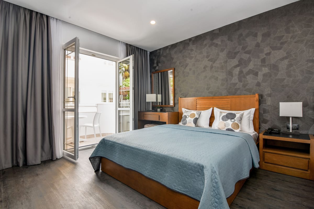 A modern bedroom with a large bed, wooden headboard, and a view through a glass door to an outdoor area.