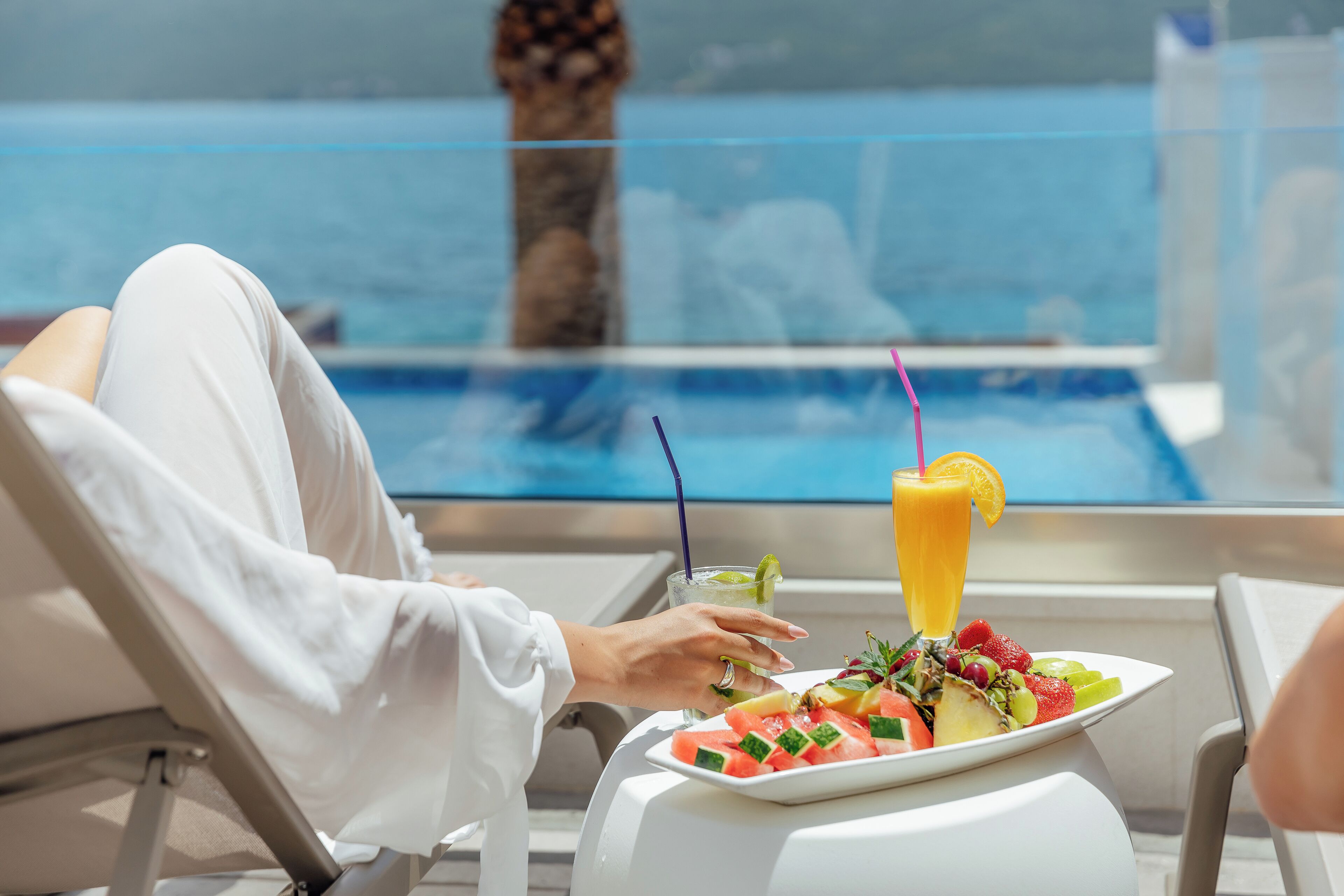 Eine Person entspannt an einem Pooltisch, neben einem Teller Obstsalat und einem Glas Orangensaft.