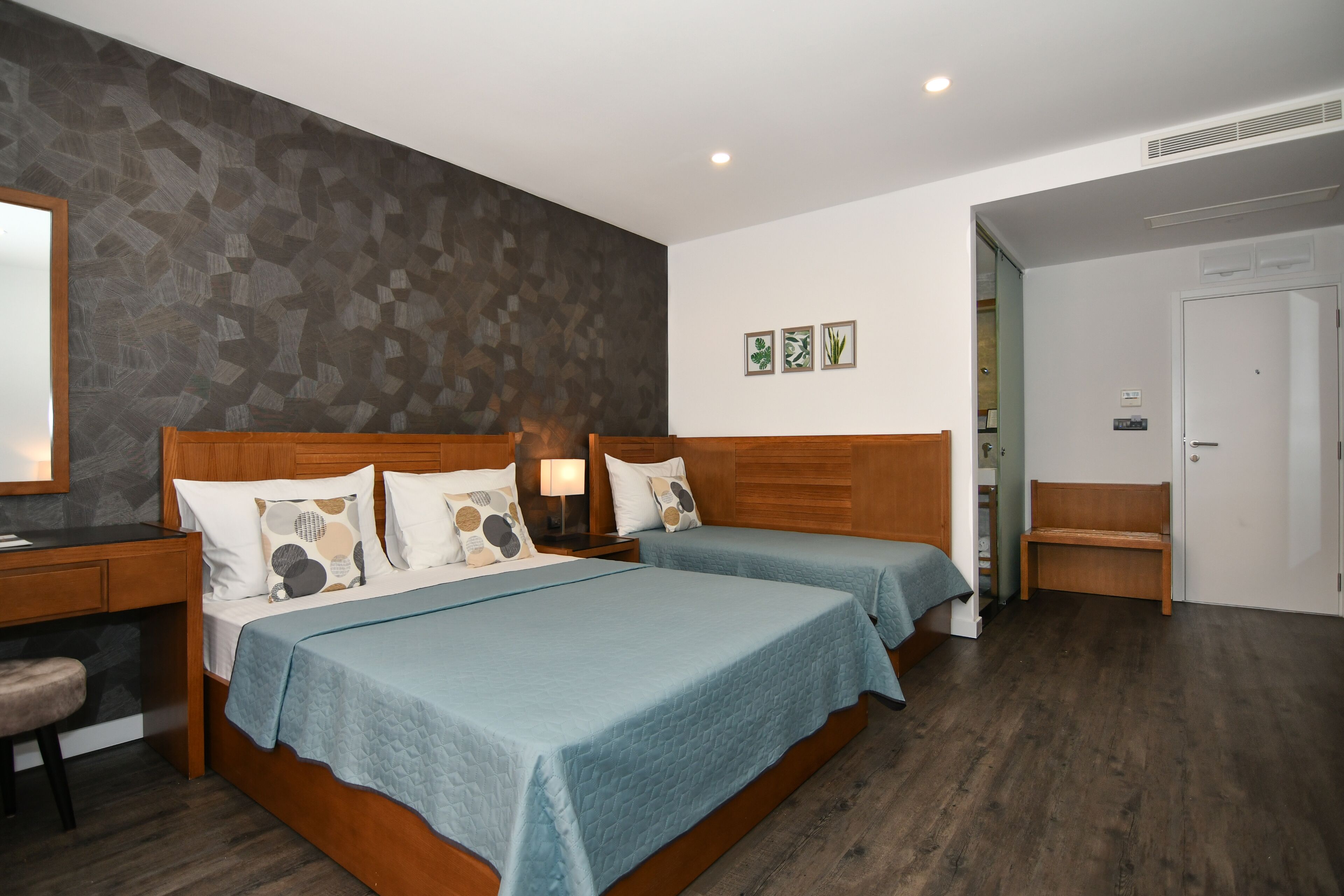 Une chambre d’hôtel avec deux lits, une tête de lit en bois, un bureau avec une chaise et un miroir.
