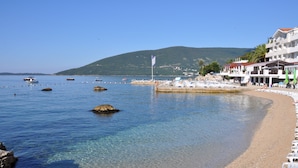 A coastal hotel with a beach, clear water, and a mountain in the background. - Hotel Perla (Herceg Novi)