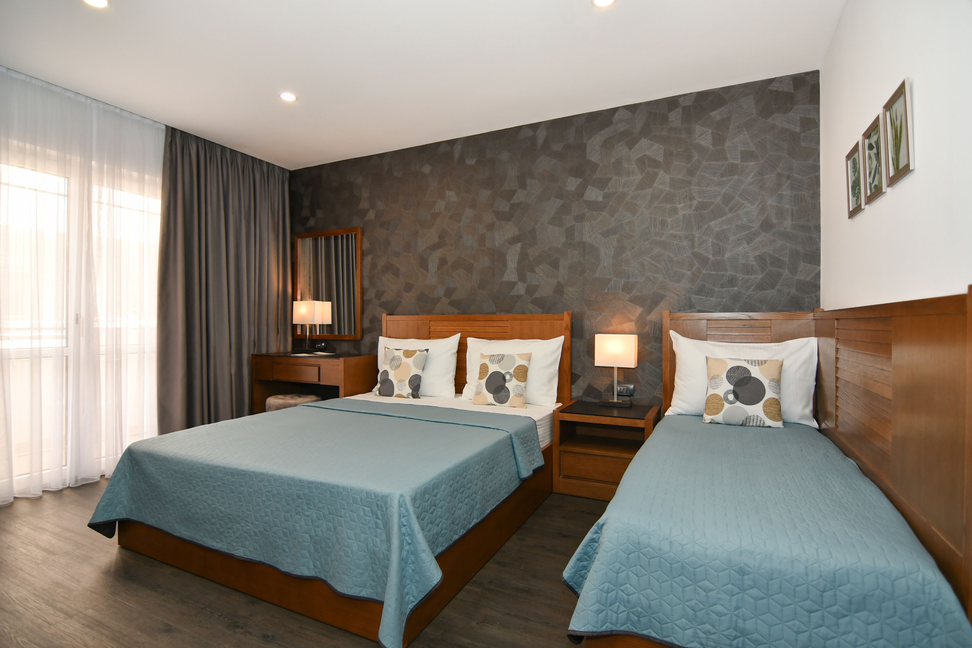 A hotel room with two beds, wooden headboards, a stone-patterned accent wall, and a large window with curtains.