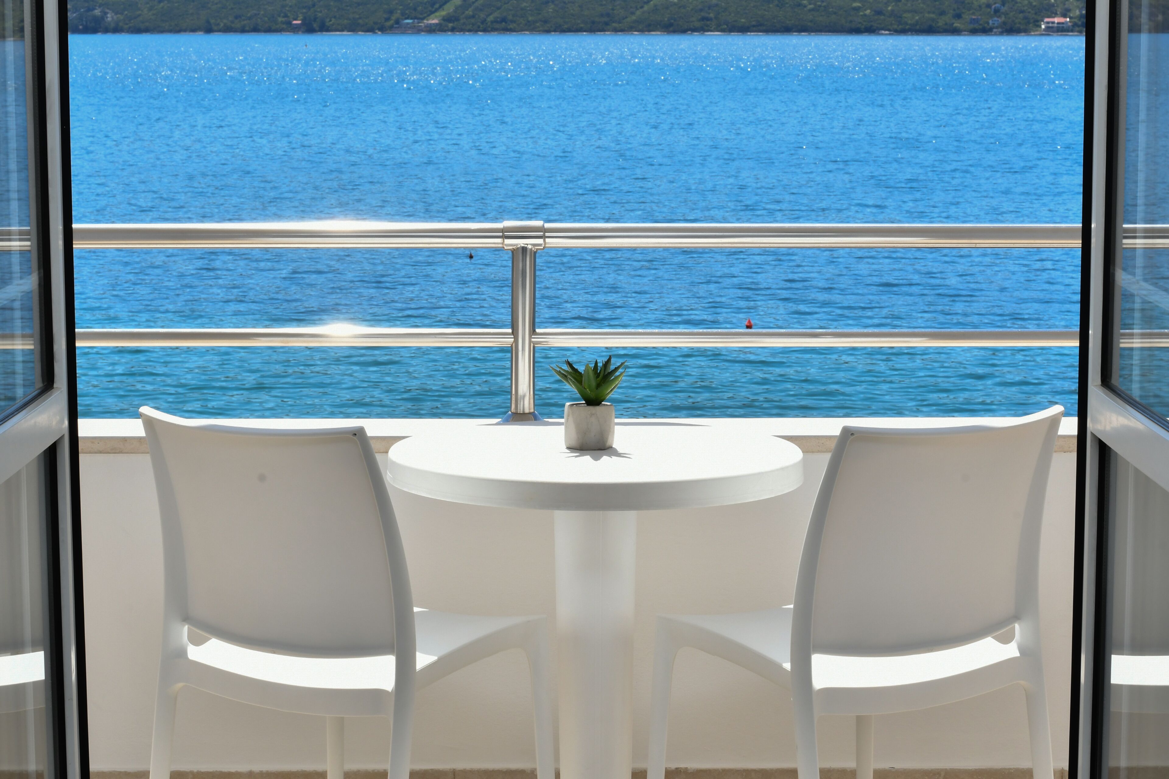 A balcony with a white table and two chairs, overlooking a body of water.