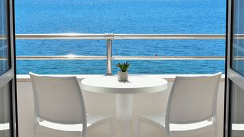 A balcony with a white table and two chairs, overlooking a body of water.
