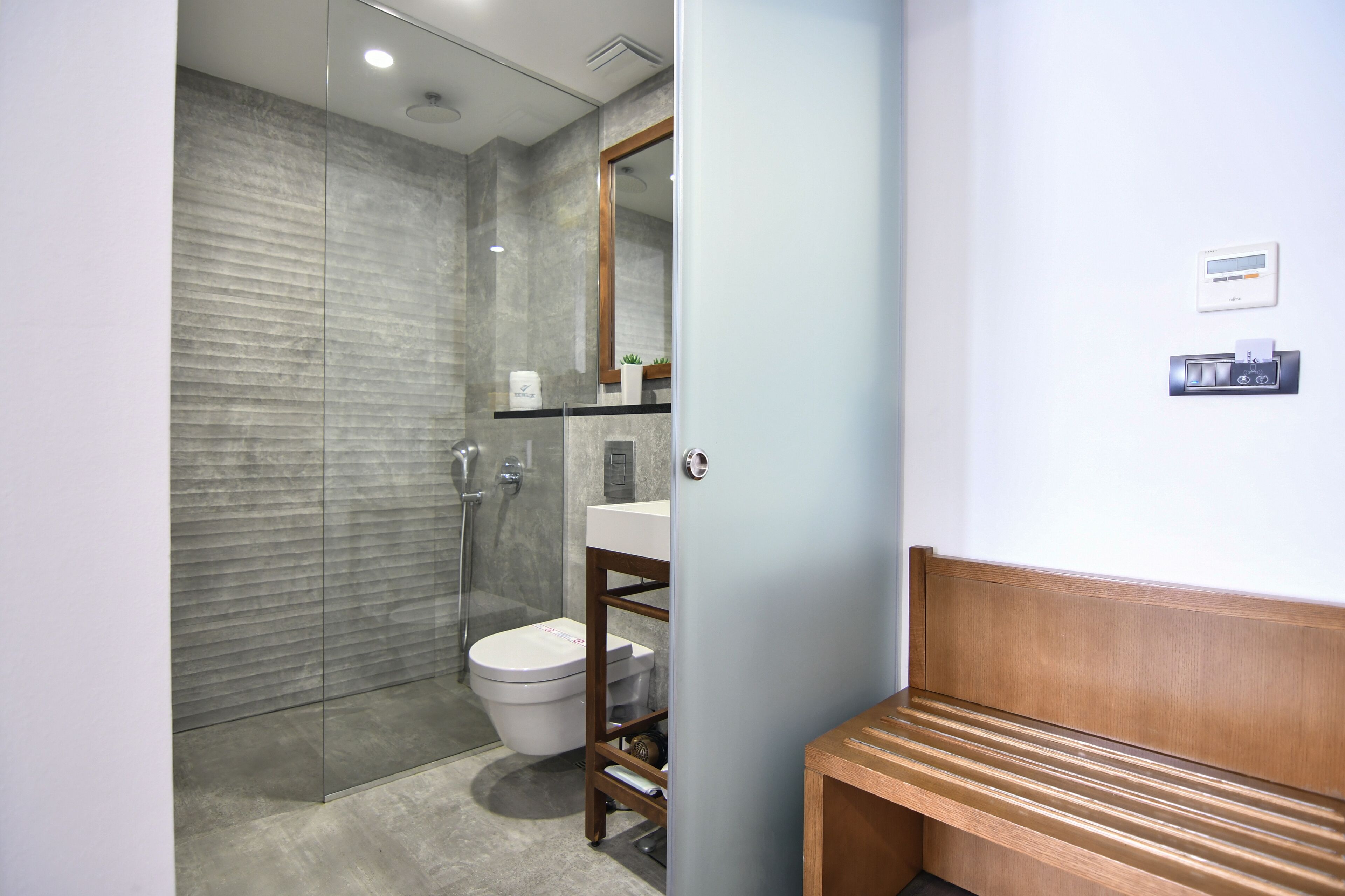 A modern bathroom with a glass shower enclosure, a toilet, and a wooden bench.