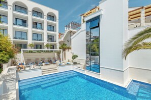 Un hotel moderno con piscina, asientos al aire libre y un edificio de varios pisos con balcones.