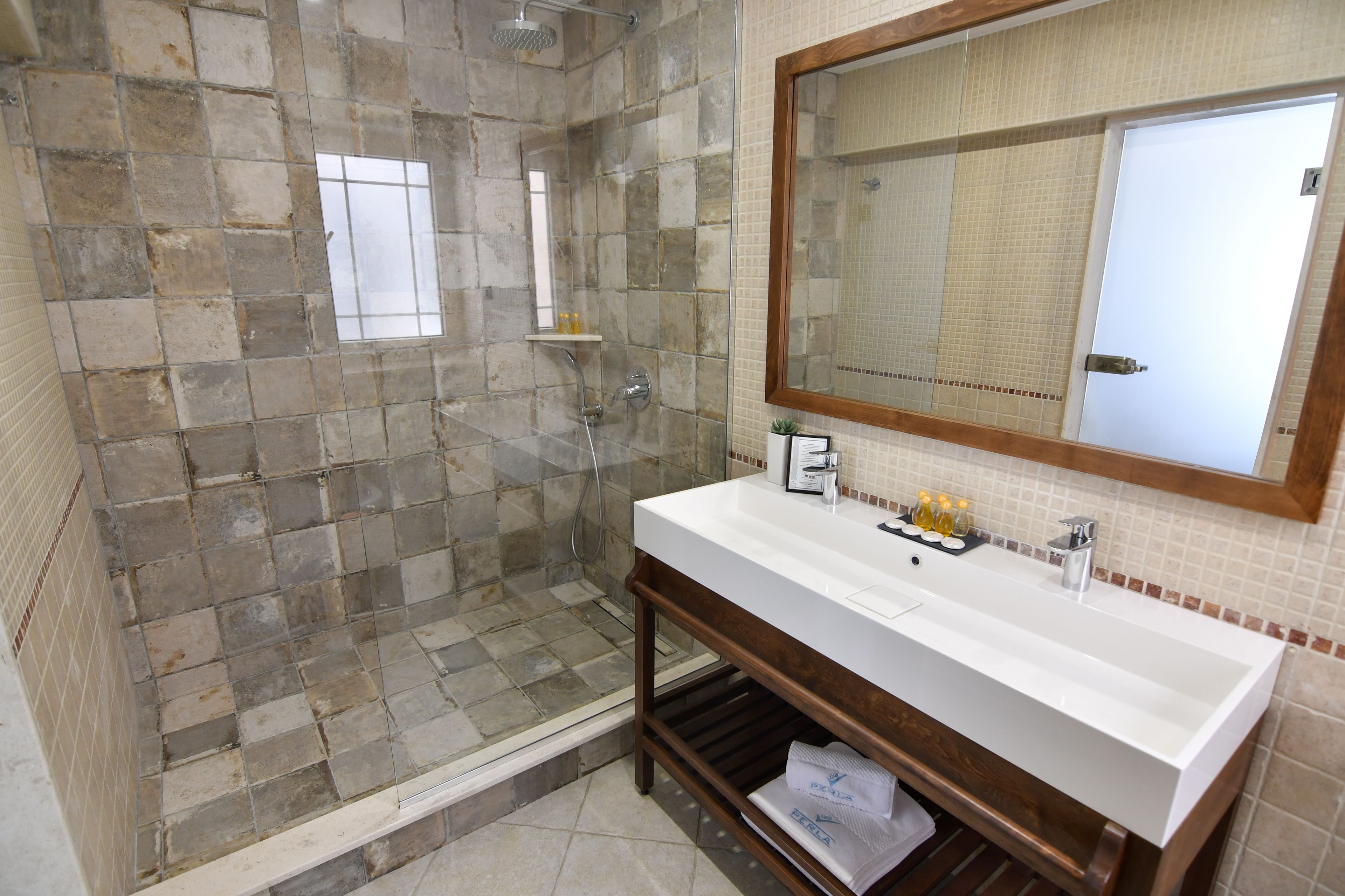 Une salle de bain avec un mur de douche en pierre, un lavabo blanc et un grand miroir.