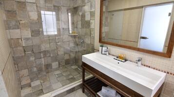 Un baño con pared de ducha de piedra, un lavamanos blanco y un espejo grande.