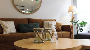 Un salón acogedor con un sofá marrón, una mesa de centro redonda de madera y dos candelabros de cristal con asas de cuerda.