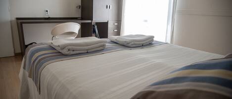 Quarto de hotel com cama, poltrona, escrivaninha e televisão na parede.