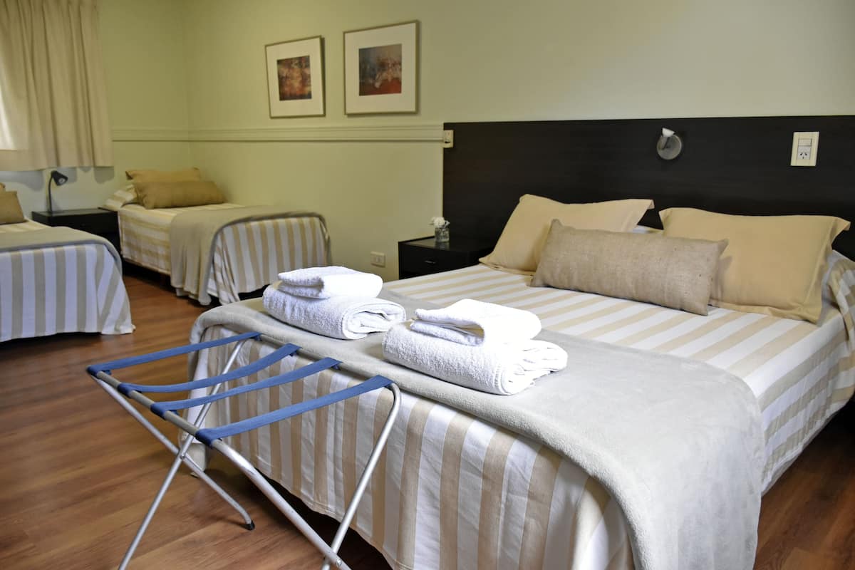 A hotel room with two single beds, a large bed, and a blue drying rack.