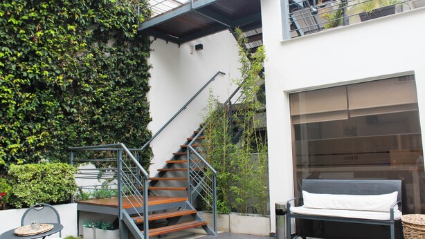 Una escalera exterior moderna con barandillas de metal, un banco y una cesta de mimbre.