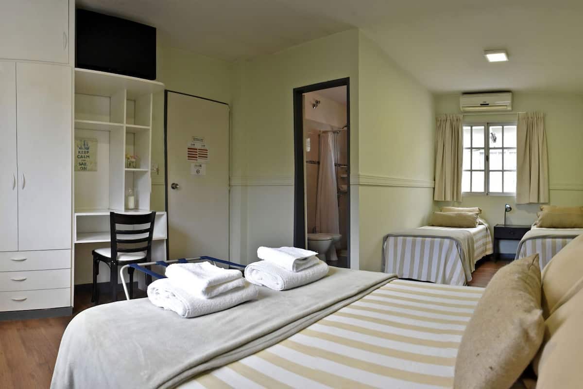 A hotel room with a bed, two bedside tables, a desk with a chair, a wardrobe, and a shower area.