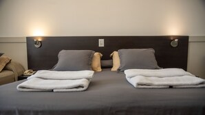 Habitación de hotel con cabecera oscura, dos almohadas, una toalla doblada y una mesita de noche con un teléfono.