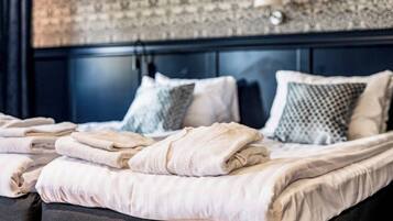 A neatly made bed with folded towels and patterned pillows in a room with a dark headboard and patterned wallpaper.