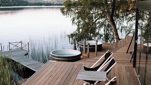 A wooden deck with a hot tub, seating area, and a view of a calm lake. - Hällsnäs (Mölnlycke)