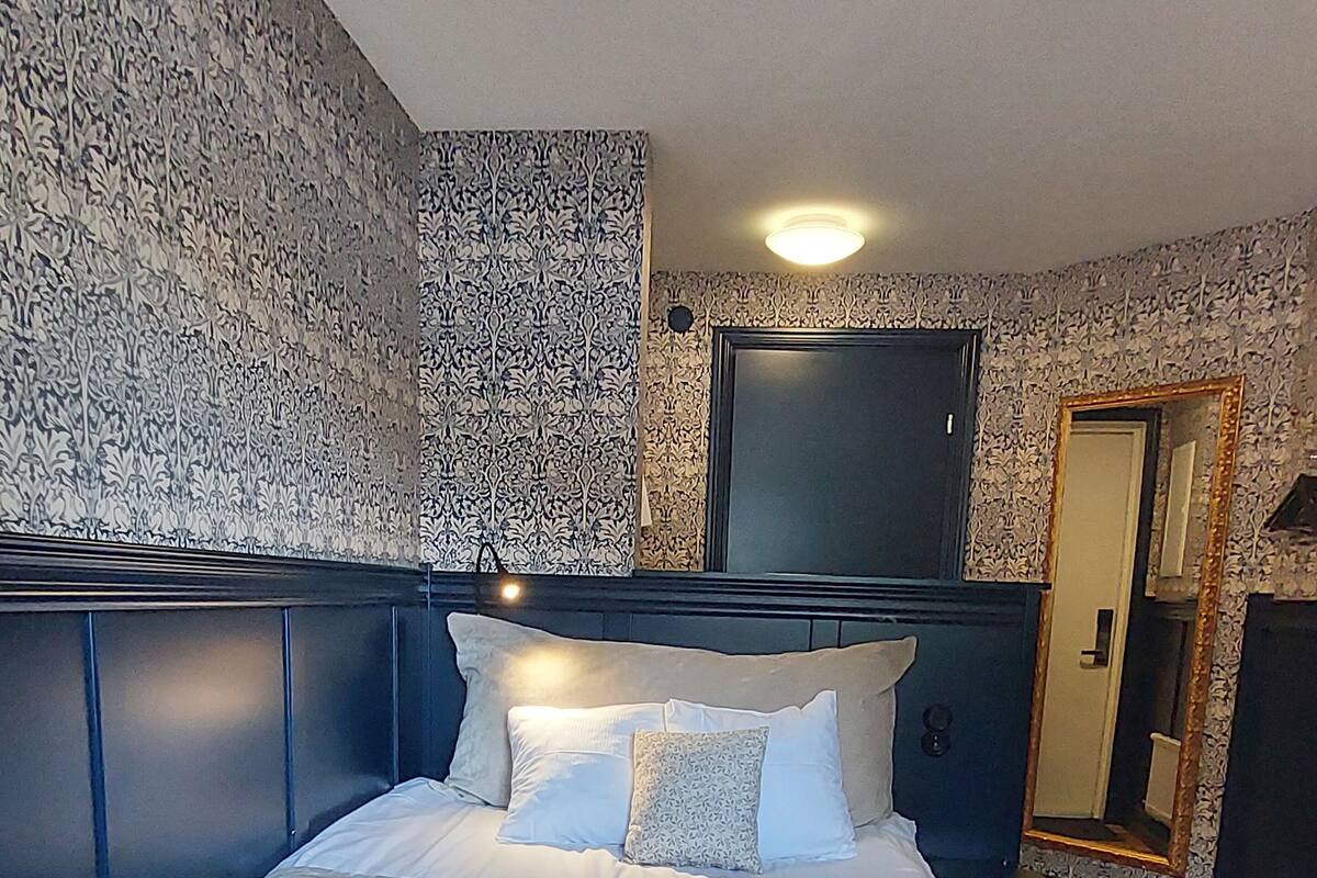 A neatly made bed with white linens and pillows, a bedside table, and a mirror on the wall.