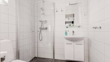 Un baño moderno con ducha acristalada, paredes de azulejos blancos, un lavabo blanco y un espejo encima.