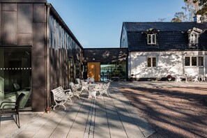 A courtyard with outdoor seating, a building with large windows, and a traditional house with a dark roof. - Hällsnäs (Mölnlycke)