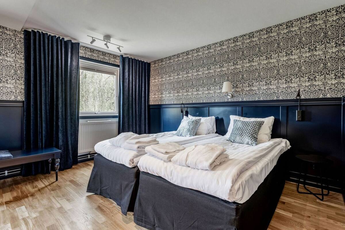 A double bed with white linens, a dark headboard, and a patterned wallpaper.
