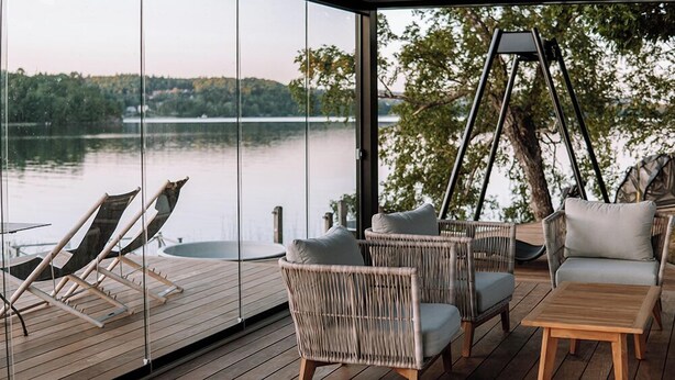 A deck with wicker furniture, a swing, and a view of a lake. - Hällsnäs (Mölnlycke)
