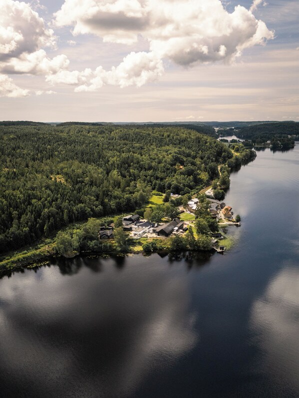 An aerial view of a lakeside community with dense forest, a small cluster of houses, and a calm lake. - Hällsnäs (Mölnlycke)