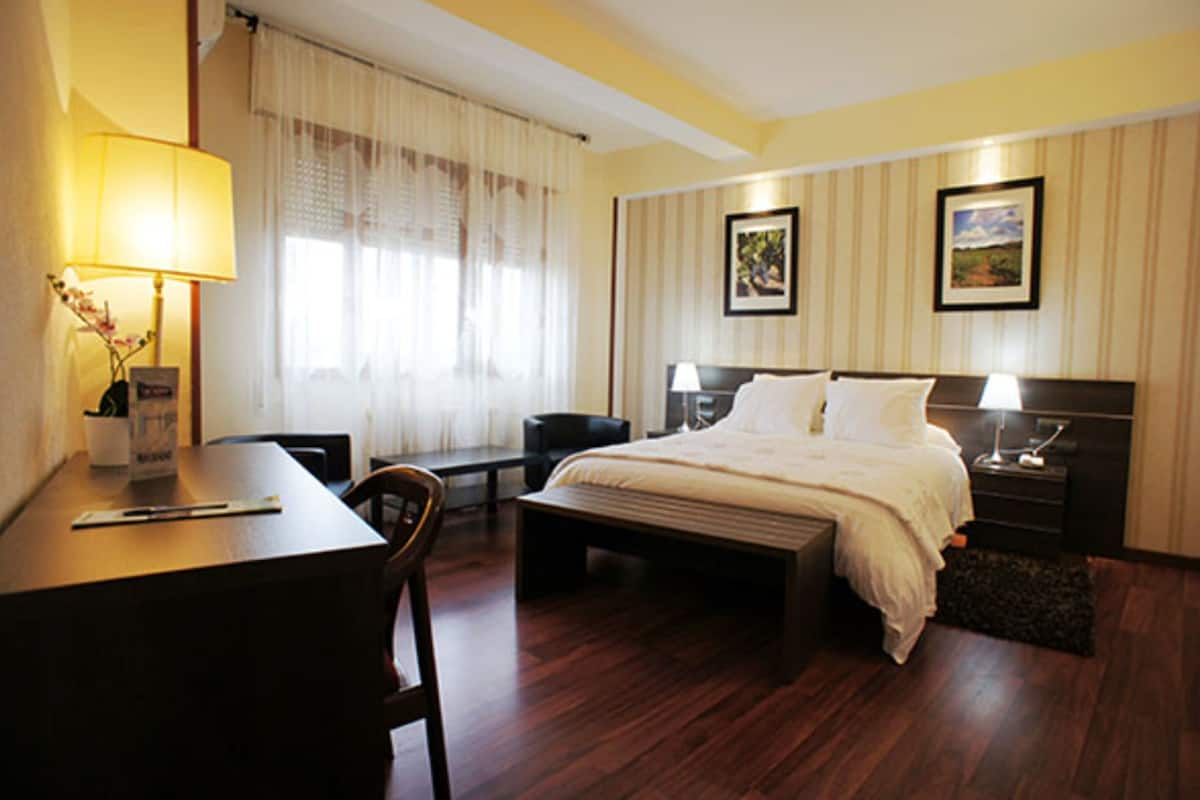 A hotel room with a bed, bedside tables, a desk, a chair, and a lamp.