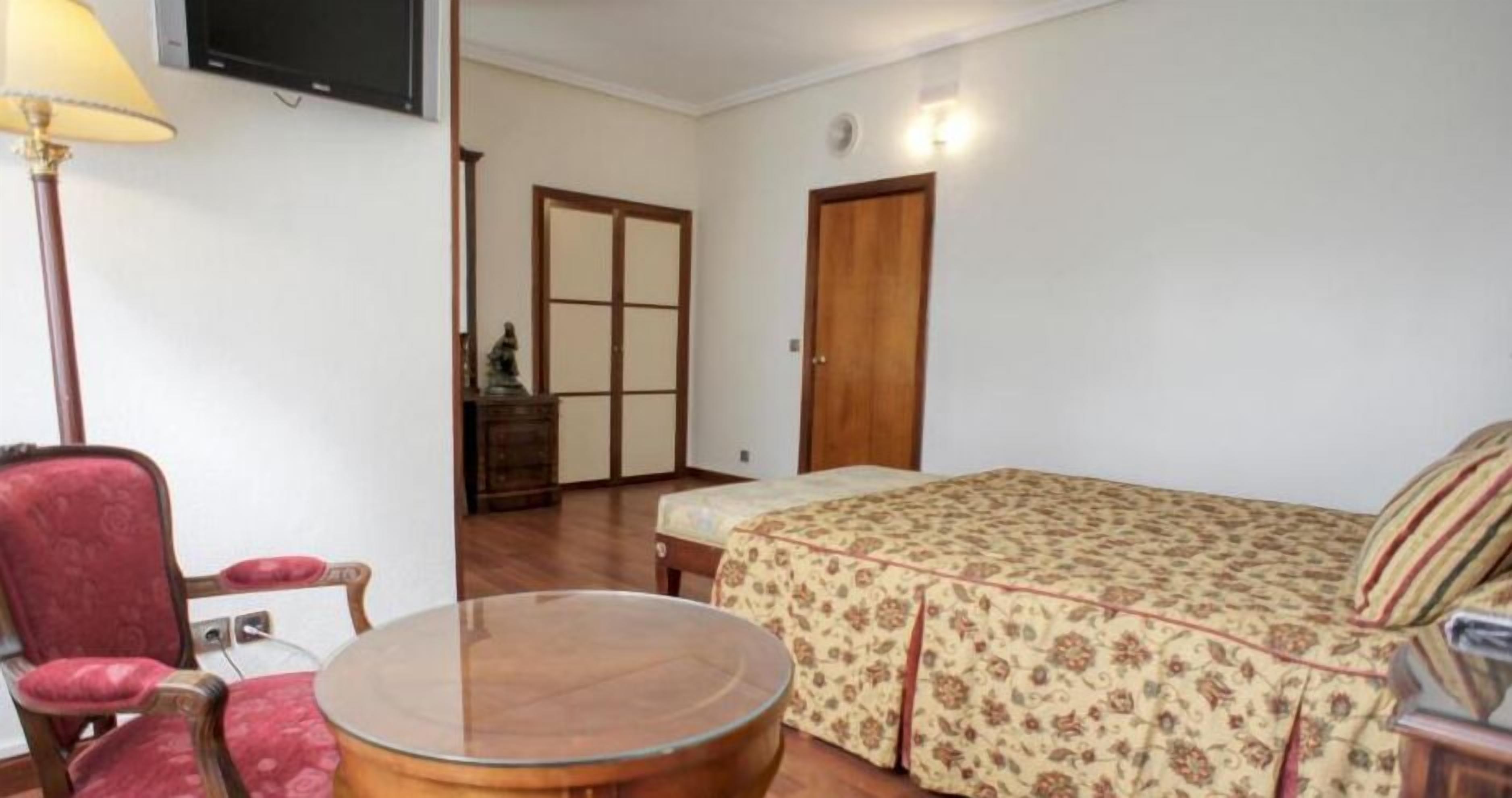 A bedroom with a bed, a chair, a table, a lamp, and a wardrobe.
