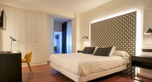 A modern bedroom with a large bed, a desk, and a chair. There is a patterned wall behind the bed and a door leading to another room. - Montermoso (Aranda de Duero)