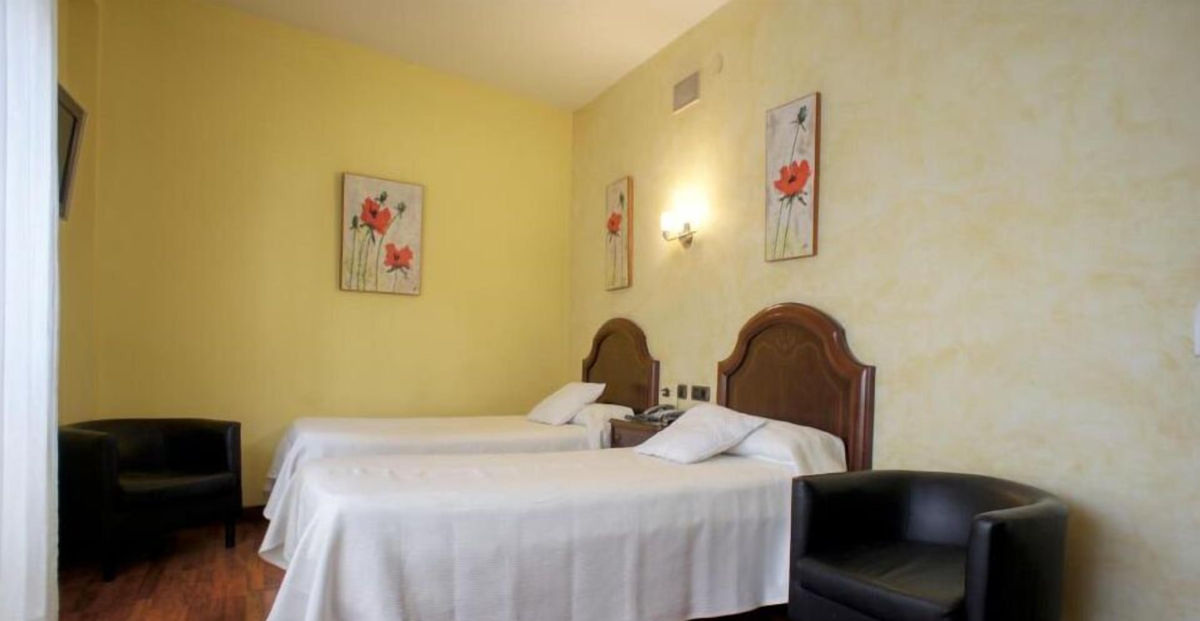 A hotel room with two single beds, a wooden headboard, a small desk, and a chair.