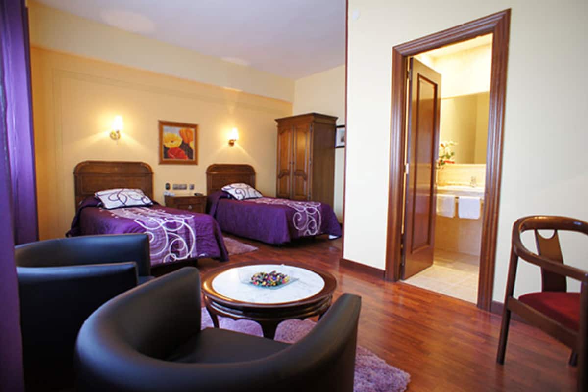 A hotel room with two beds, a round table, a chair, and a wardrobe.