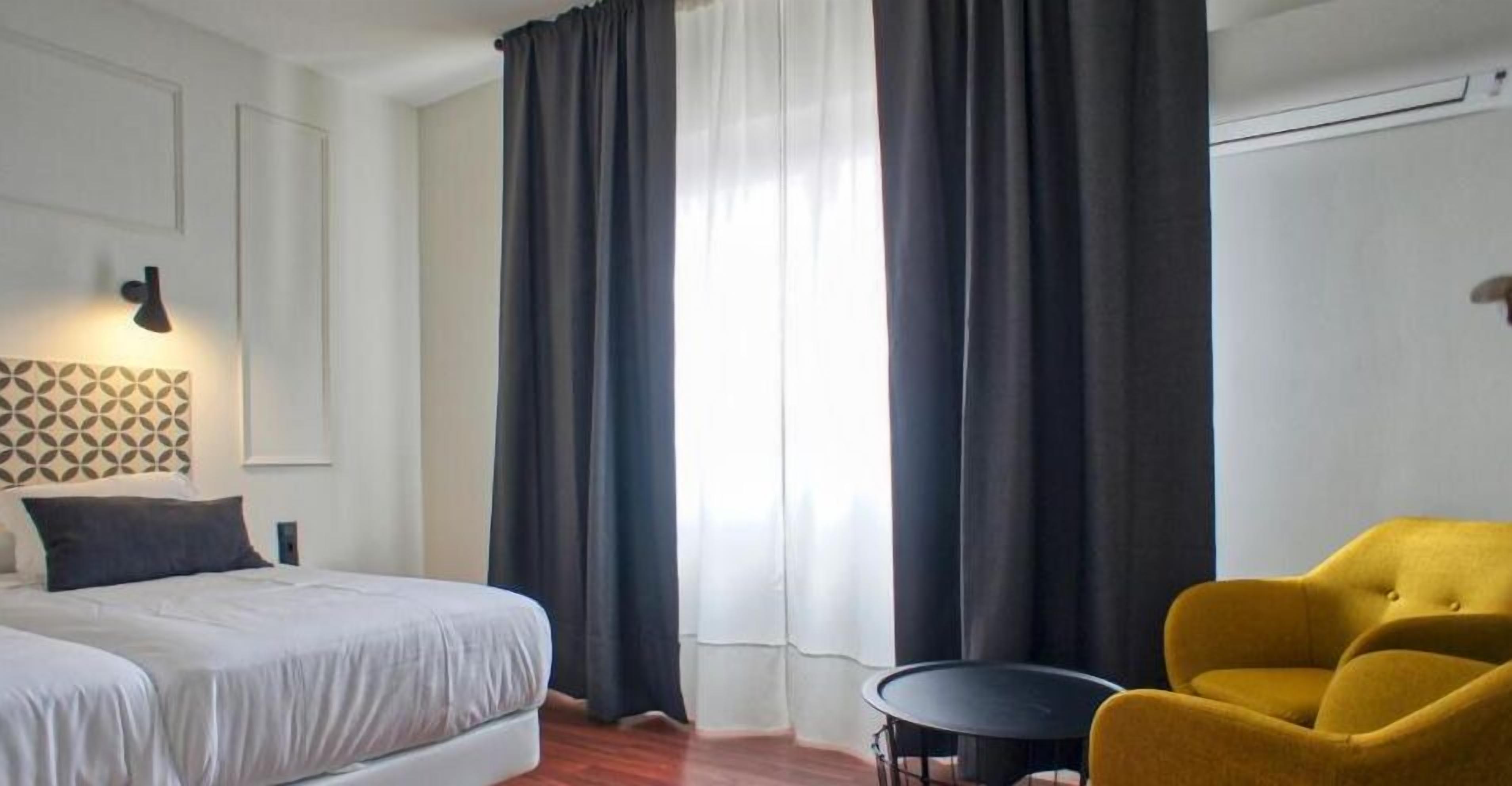 A hotel room with a bed, a small round table, and a yellow armchair.