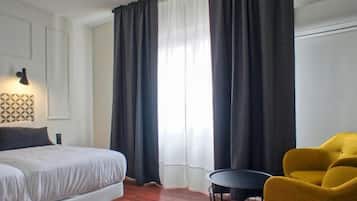 A hotel room with a bed, a small round table, and a yellow armchair.