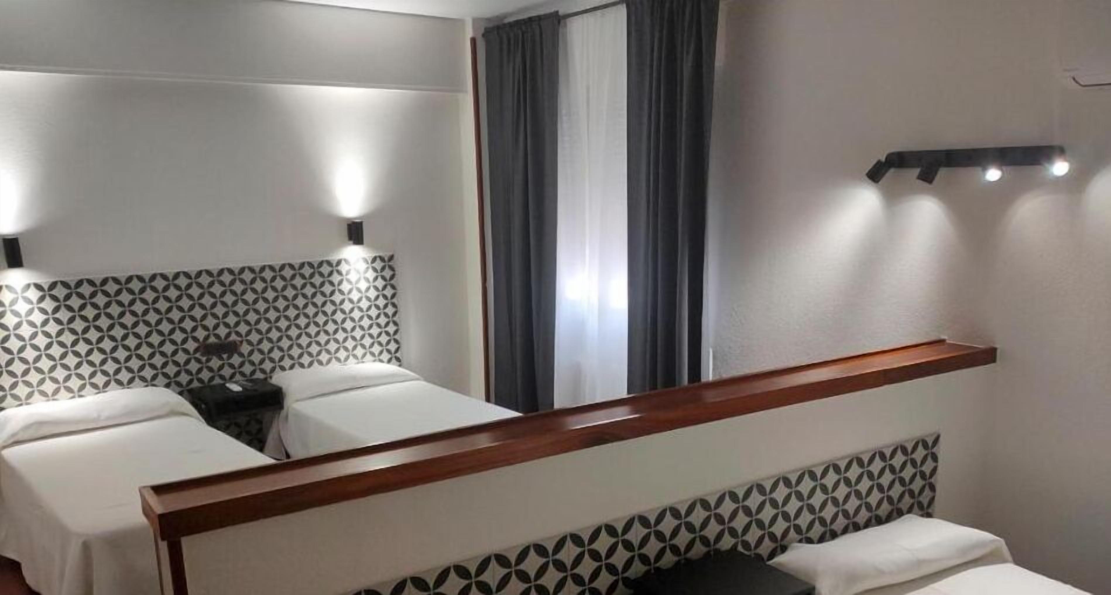 A hotel room with two beds, a wooden headboard, a nightstand, and a mirror.
