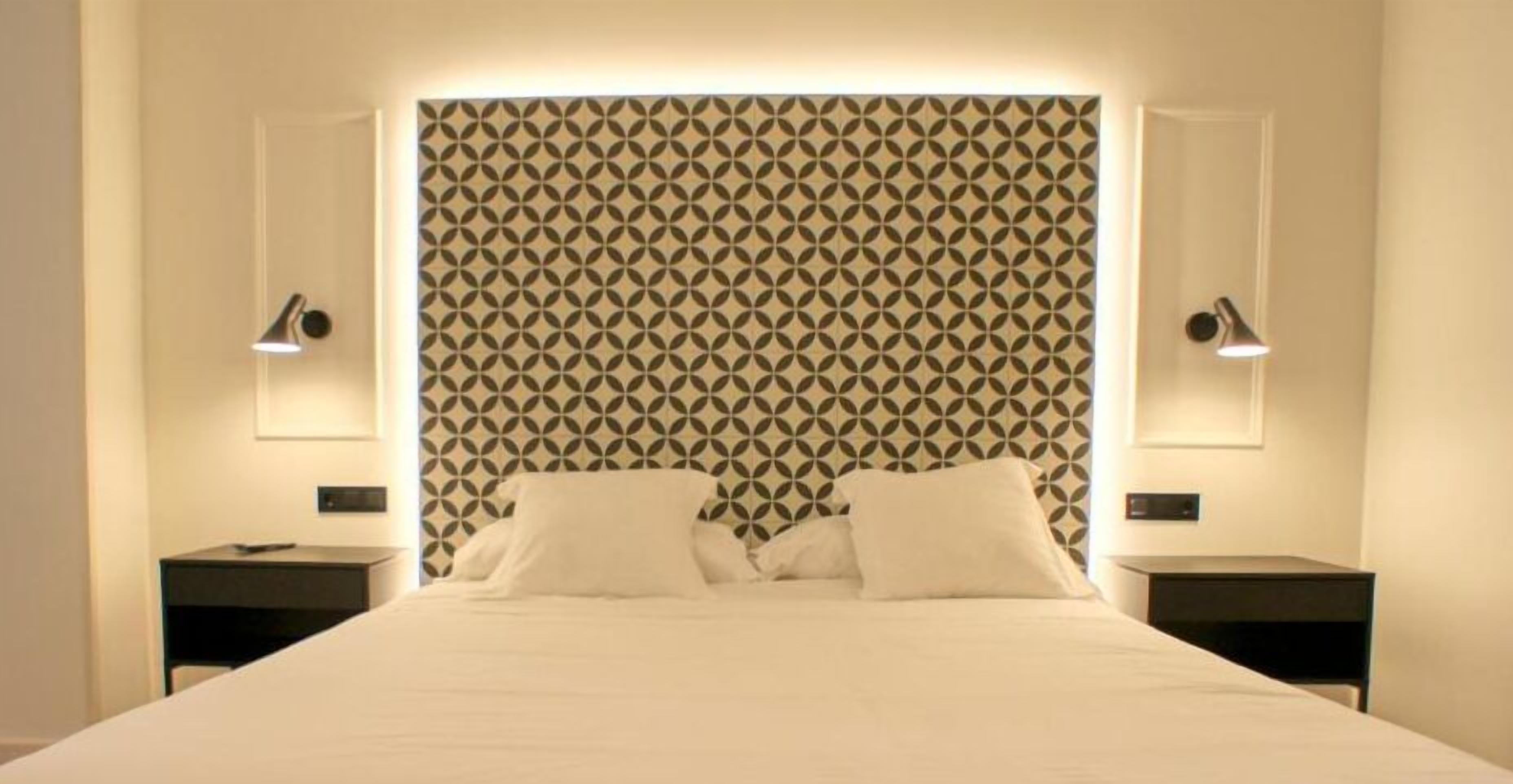 Una habitación de hotel con un cabecero estampado, dos mesitas de noche con lámparas y una cama bien hecha.