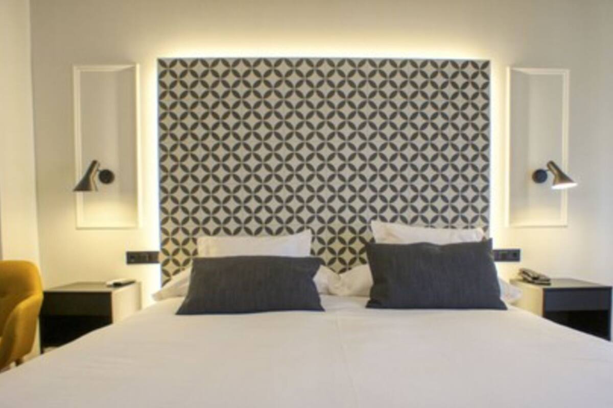 A hotel room with a bed, two bedside tables, a lamp, and a patterned headboard.