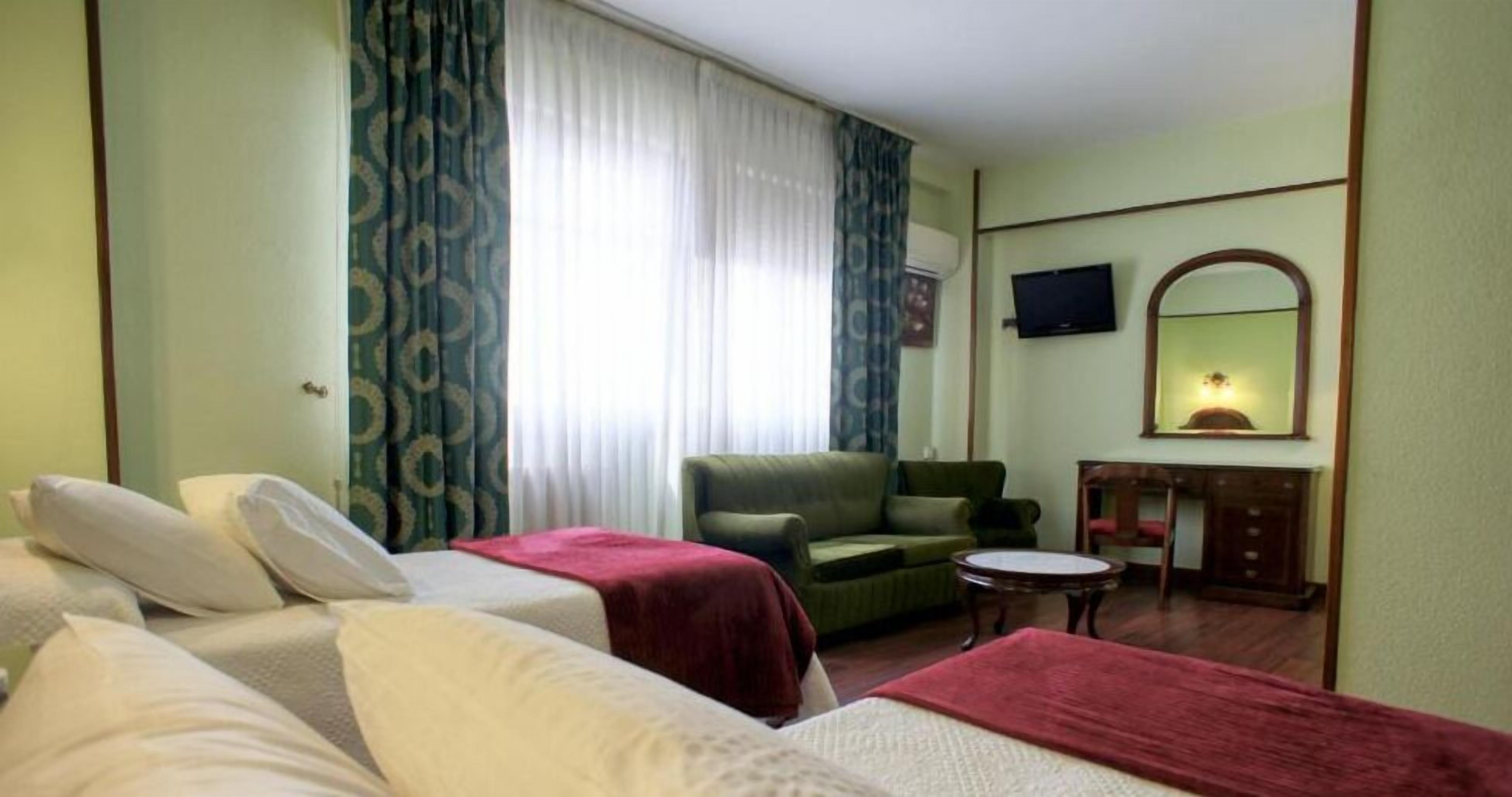 Ett hotellrum med två sängar, en grön soffa, ett litet runt bord, en tv och en spegel.