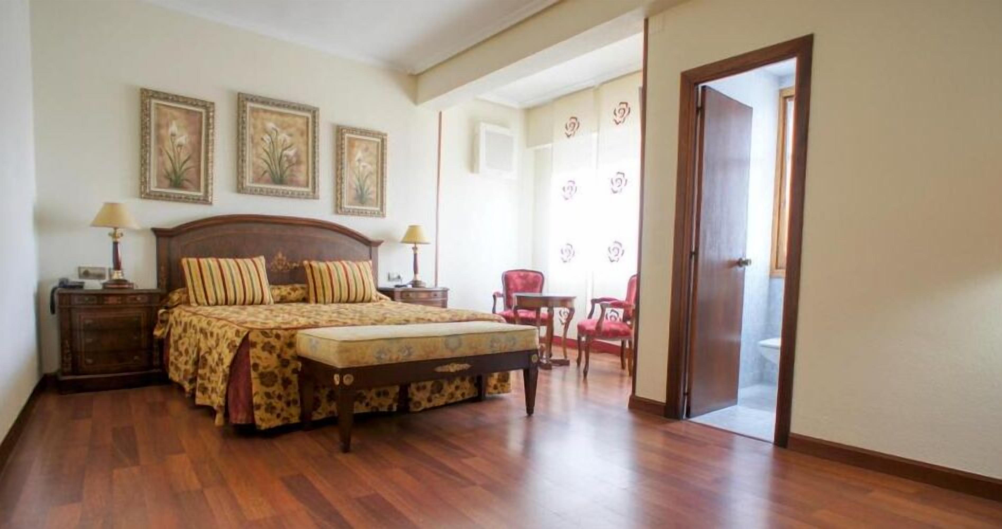 Un dormitorio con una cama de madera, una mesita de noche, una silla y una puerta que da a otra habitación.