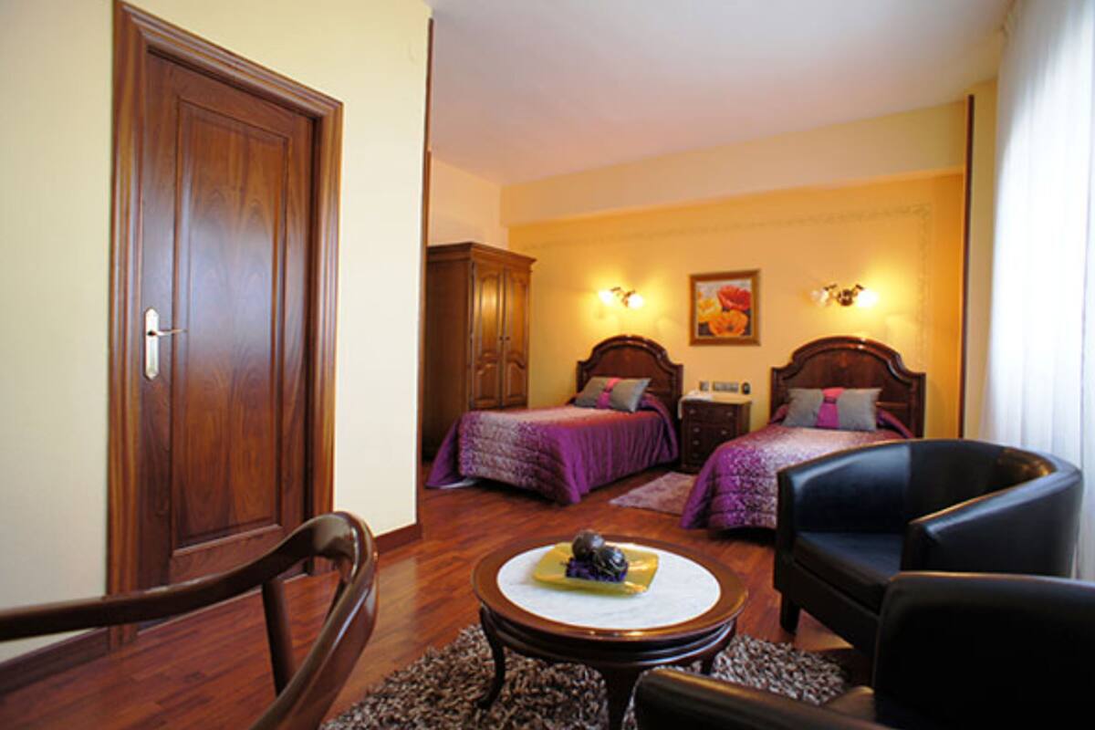 A room with two beds, a wooden wardrobe, a round table with a decorative item, and a black armchair.
