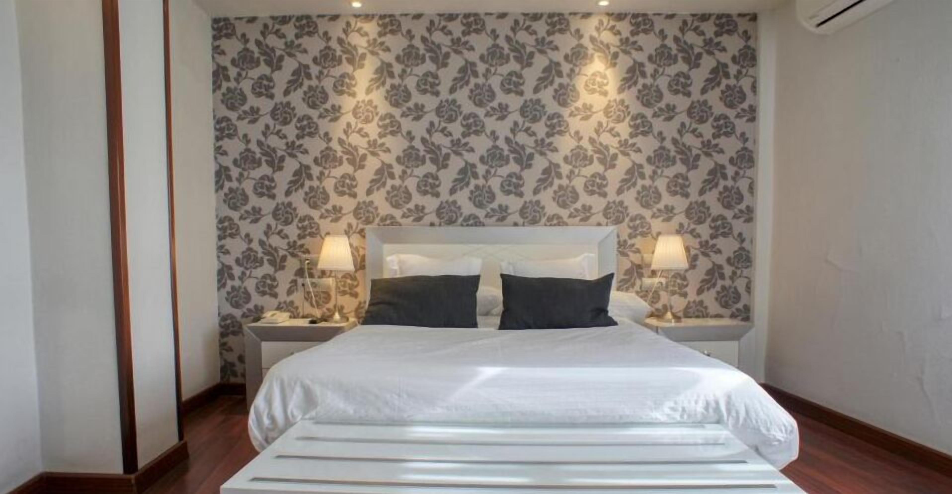 A neatly arranged bedroom with a large bed, two bedside tables, and a floral-patterned wallpaper.