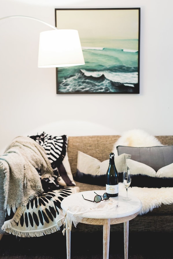 A cozy living room with a sofa, a round coffee table, a bottle of wine, and a glass of wine.