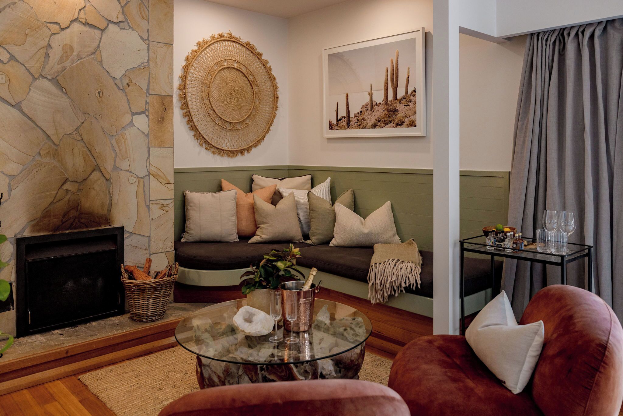 A living room with a stone wall, a fireplace, a sofa with cushions, a glass coffee table, and a red armchair.