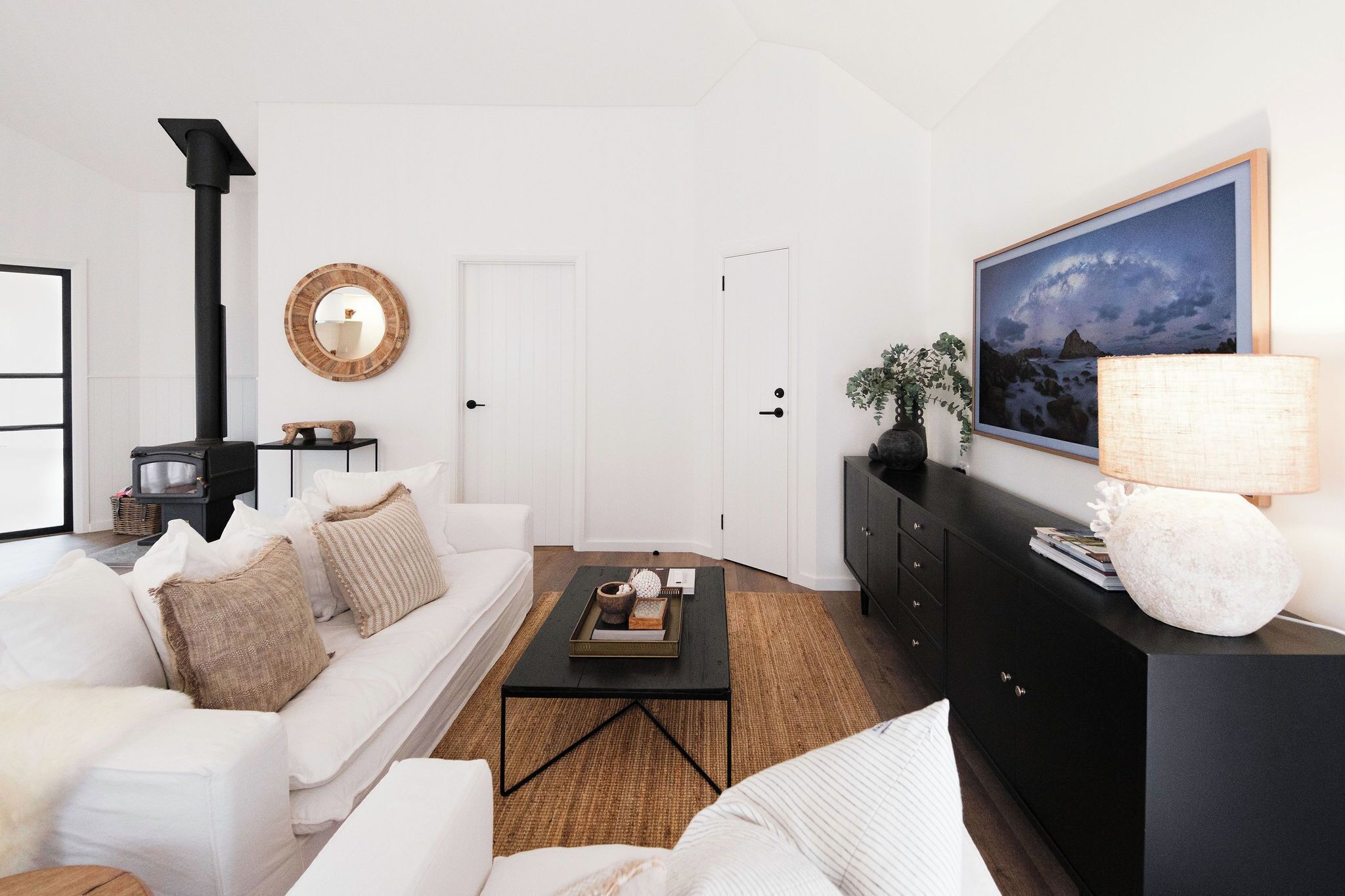 Un salón moderno con un sofá blanco, una mesa de centro negra y un mueble negro con un cuadro enmarcado.