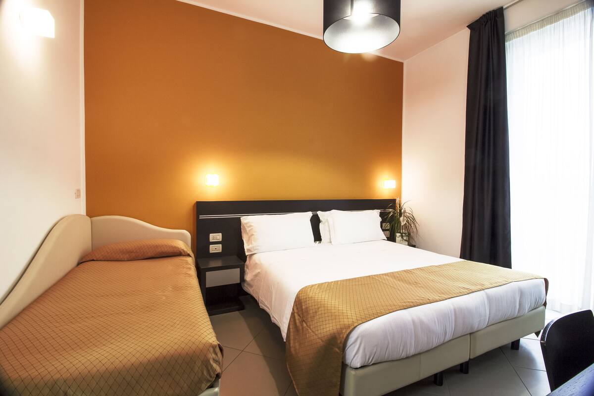 A hotel room with a bed, a bedside table, a chair, and a window with curtains.