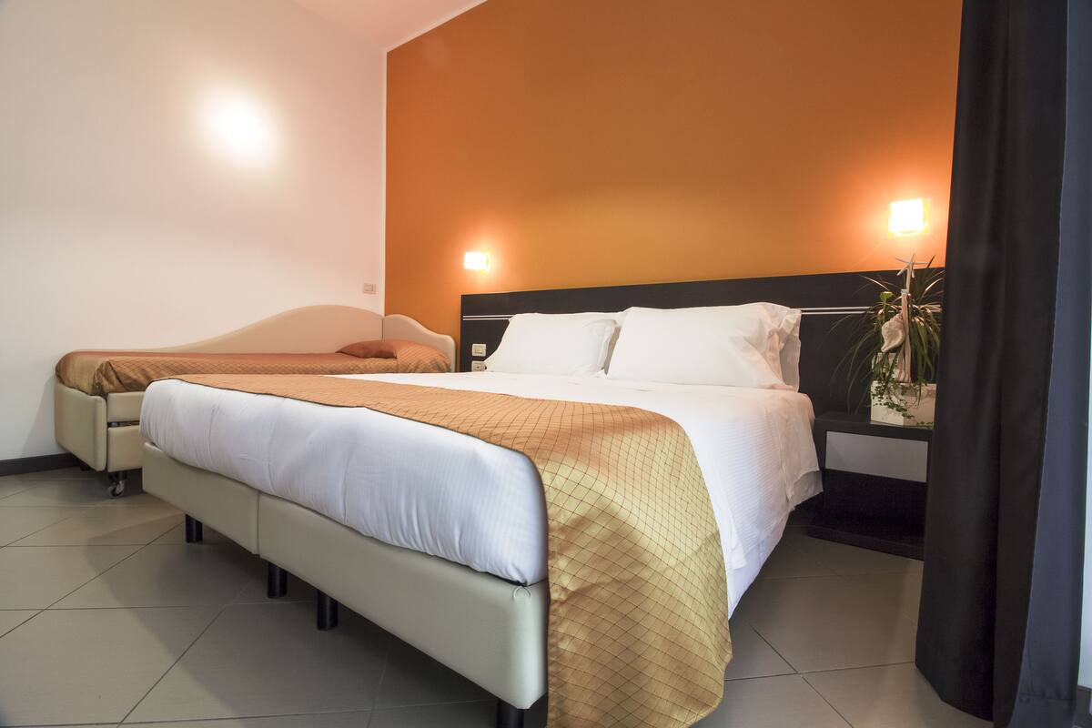 A hotel room with a large bed, a smaller bed, and a nightstand with a plant.