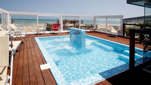 A rooftop pool with a view of the beach, surrounded by lounge chairs and a table. - Panama Majestic (Rimini)