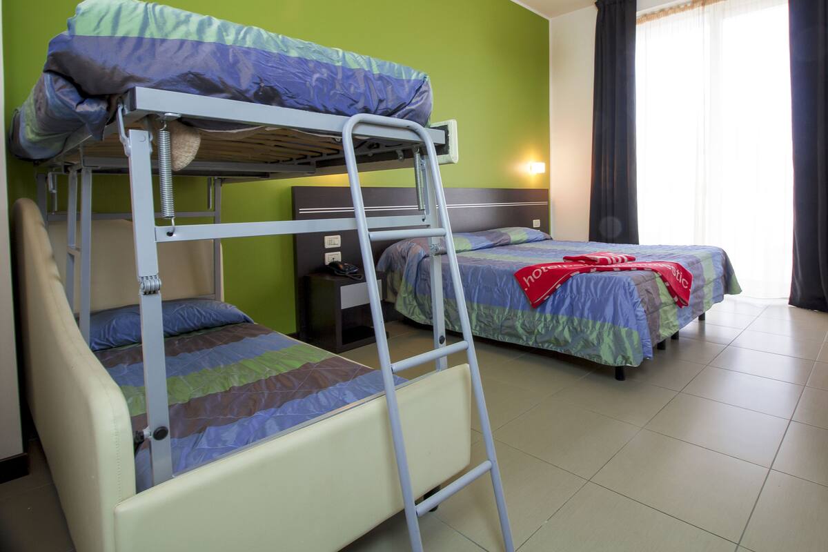 A bunk bed room with a ladder, a nightstand, and a bed with a red blanket.
