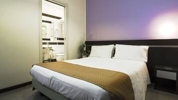 Een netjes ingerichte hotelkamer met een groot bed, een nachtkastje en een badkamer zichtbaar door een geopende deur.
