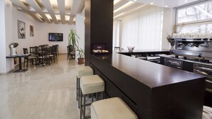 A modern kitchen with a dark countertop, bar stools, a flat-screen TV, and a coffee machine. - Panama Majestic (Rimini)