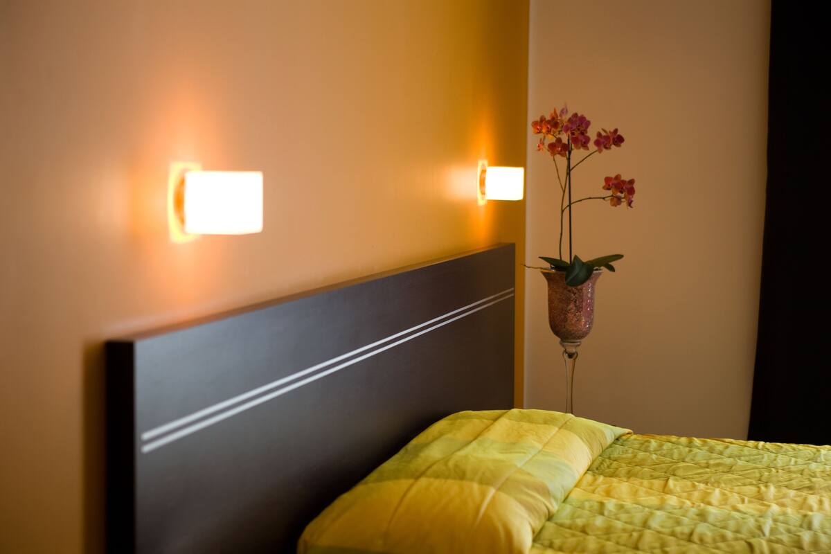 A hotel room with a bed, a nightstand, and a wall-mounted light fixture.